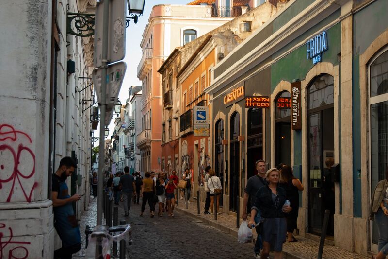 Rua estreita do Bairro Alto em Lisboa com bares, néons e movimento de pessoas ao entardecer